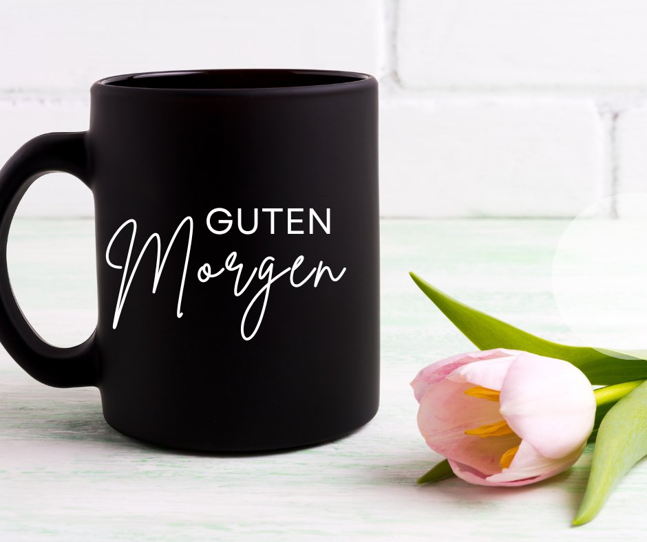 Einen Schönen Guten Morgen Bilder mit einer eleganten schwarzen Kaffeetasse und einer zarten rosa Tulpe auf einem hellen Holztisch, perfekt für einen friedlichen Morgenstart.